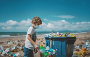 Niño de pie en la playa junto a residuos de plástico